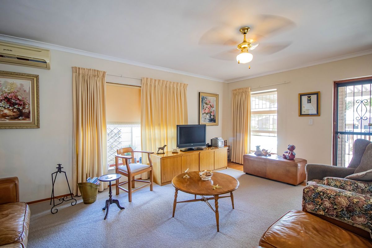 A comfortable living room featuring carpeted flooring, a ceiling fan, and a wall-mounted split system air conditioner.
