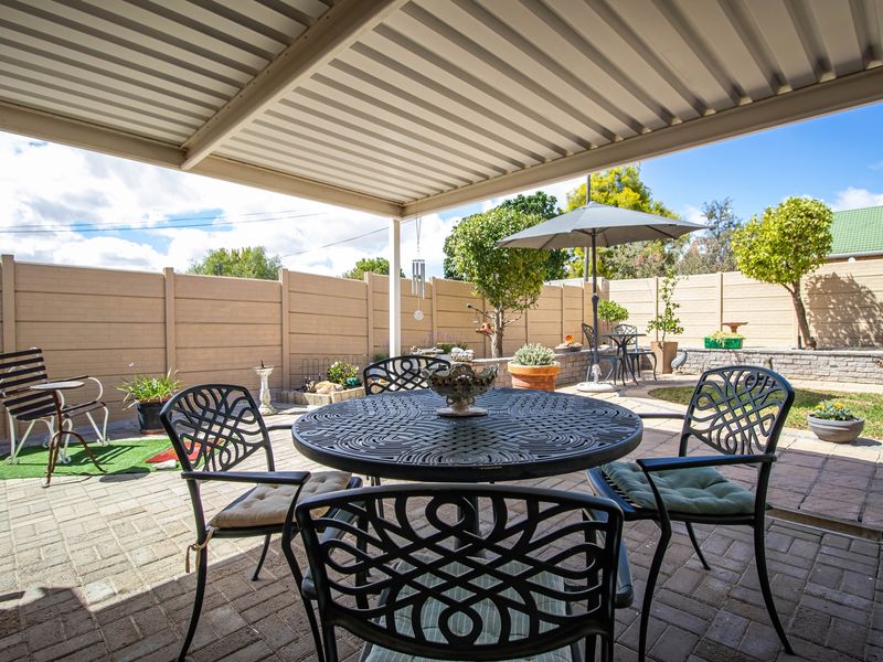 A covered outdoor patio area featuring paved flooring and a corrugated metal roof, overlooking a private garden with a retaining wall.