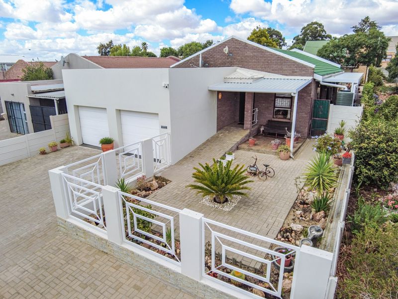 Aerial view of a well-maintained residential property featuring a double garage, paved driveway, secure perimeter fencing, and a covered front patio area.
