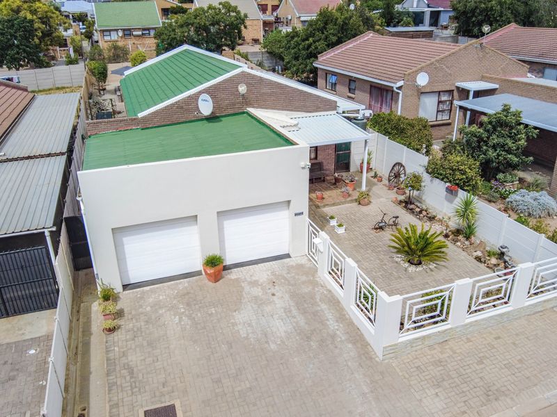 Aerial view of a residential property featuring a double garage, paved driveway, secure boundary wall, and a low-maintenance landscaped courtyard area.