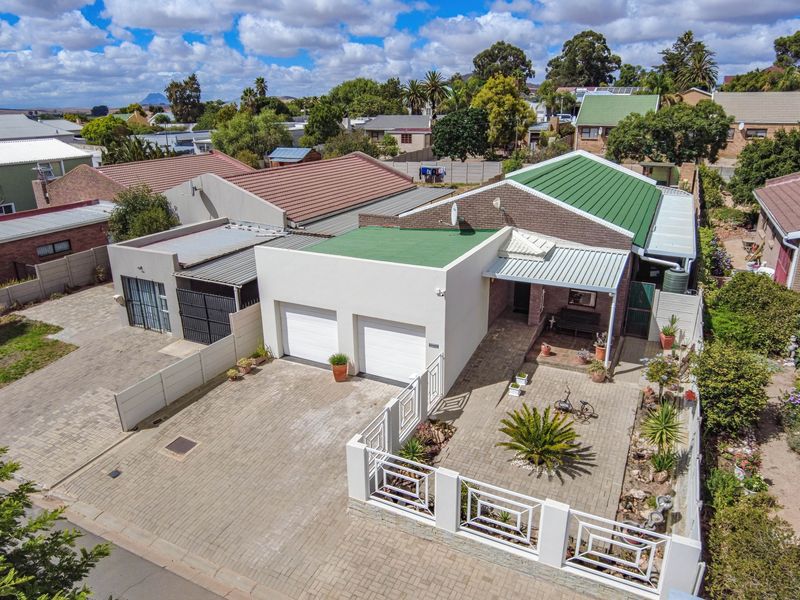 Aerial view of a residential property featuring a double garage, paved driveway, covered patio, and well-maintained exterior finishes in a suburban setting.