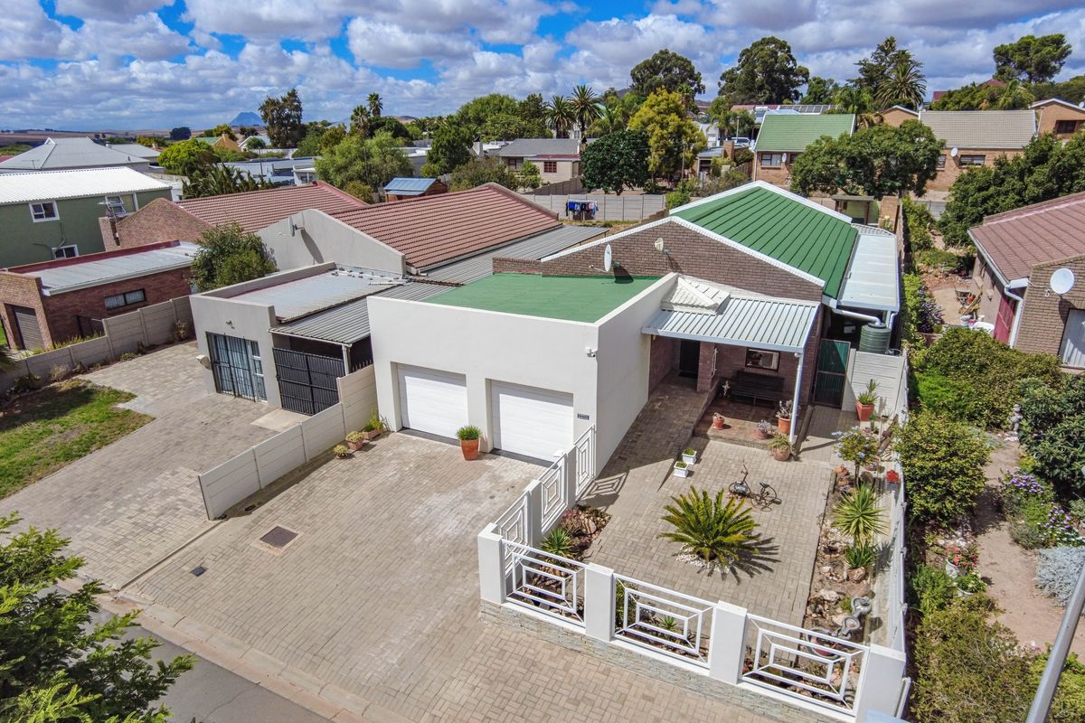 Aerial view of a residential property featuring a double garage, paved driveway, covered patio, and well-maintained exterior finishes in a suburban setting.