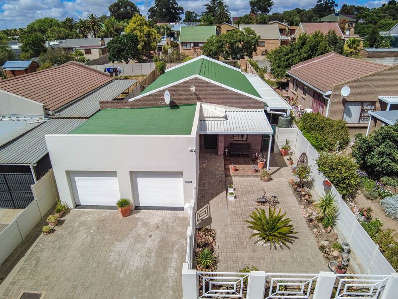 Aerial view of a residential property featuring a double garage, paved driveway, and a covered patio area within a fenced garden setting.