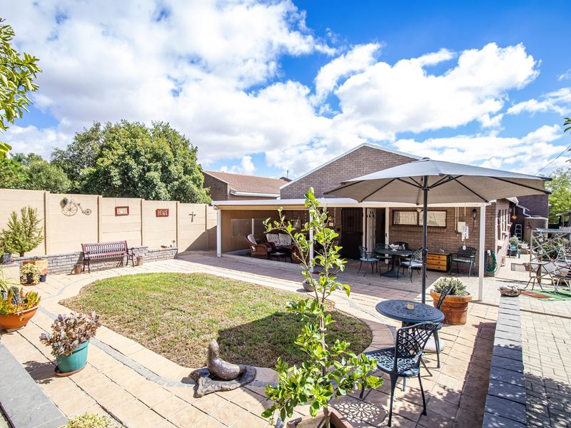 A well-maintained rear garden featuring a paved patio area, a covered outdoor space, and a brick boundary wall.