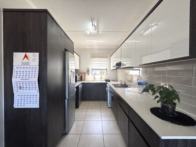 Modern galley-style kitchen featuring sleek dark cabinetry, stone countertops, a gas hob, extractor fan, and tiled flooring with a neutral backsplash.