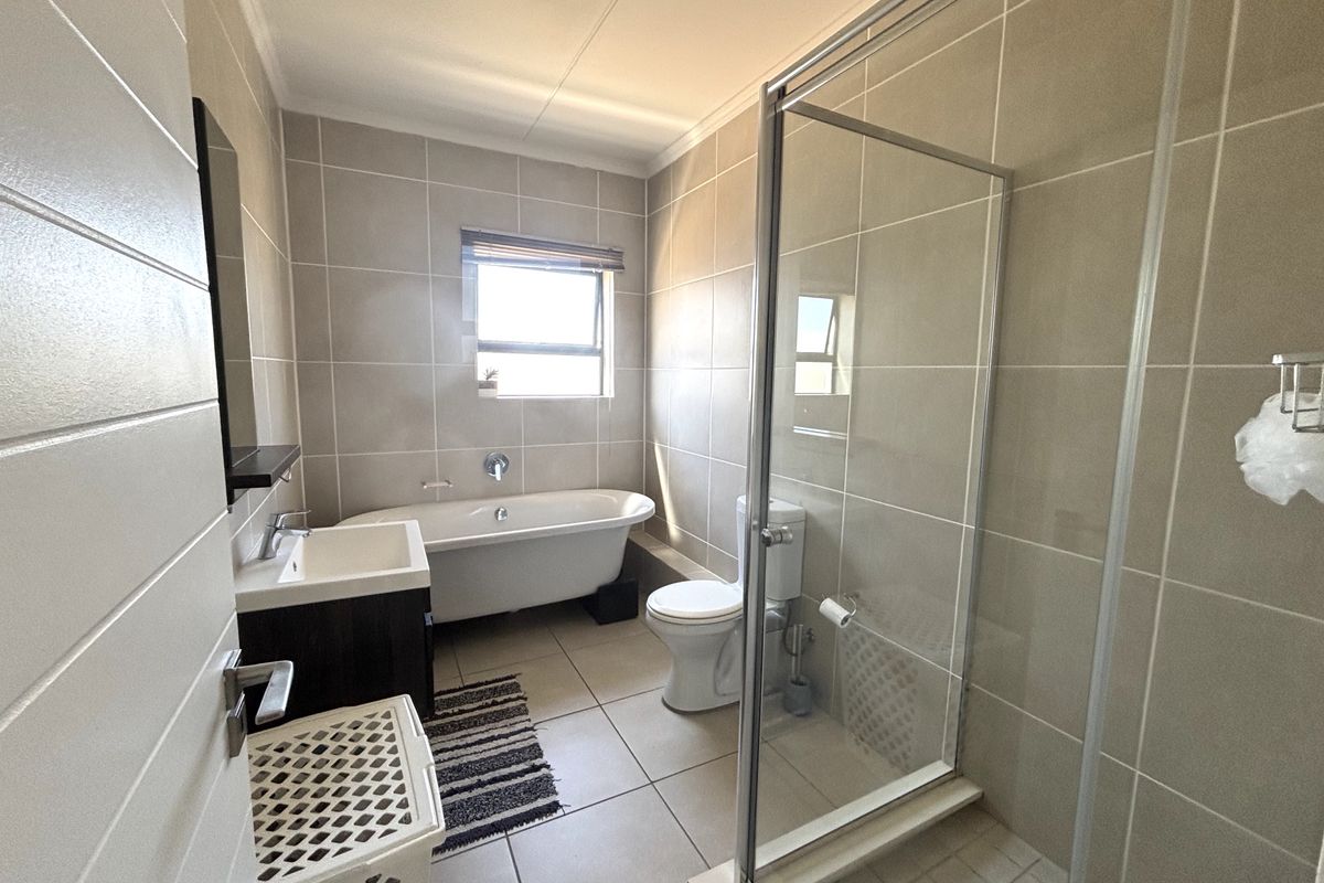 Modern bathroom featuring a freestanding bathtub, separate glass shower enclosure, vanity unit, and neutral wall and floor tiling.