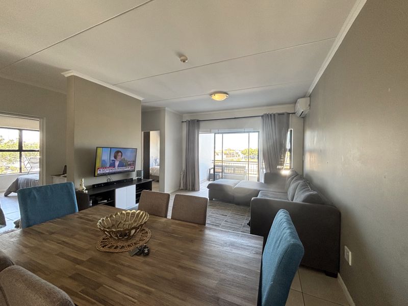 Spacious open-plan living and dining area featuring tiled flooring, air conditioning, and direct access to a private balcony through sliding glass doors.