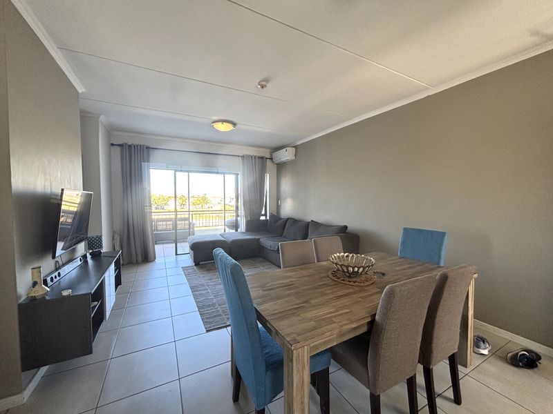 Open-plan living and dining area featuring tiled flooring, a split-system air conditioner, and large sliding glass doors leading to an outdoor balcony.