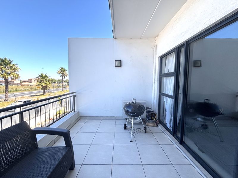 A spacious balcony featuring tiled flooring, a metal balustrade, and large sliding glass doors, offering an ideal outdoor space for relaxation.