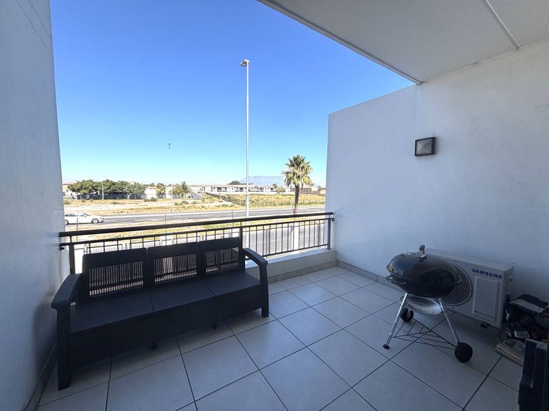 A spacious covered balcony featuring tiled flooring, a metal balustrade, and an integrated air conditioning unit, offering clear views of the surrounding area.