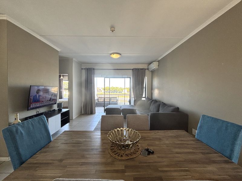 Open plan living and dining area featuring tiled floors, an air conditioning unit, and large sliding glass doors leading to a balcony.