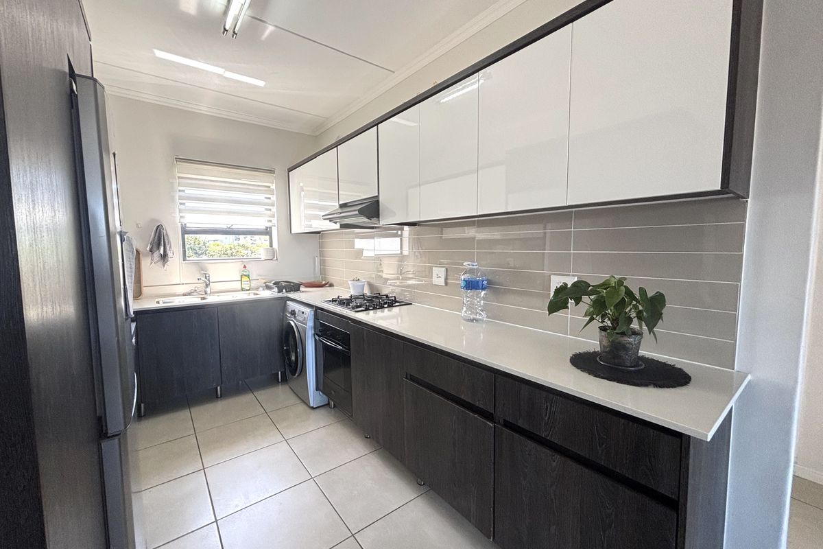 Modern galley-style kitchen featuring sleek dark wood lower cabinets, white upper cabinetry, stone countertops, gas hob, and integrated laundry appliances.