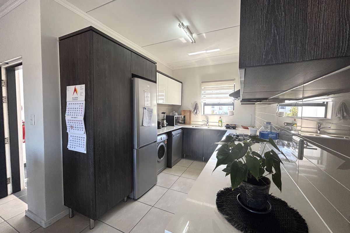 A modern kitchen featuring dark wood cabinetry, stone countertops, tiled flooring, and integrated appliances, offering a functional and well-maintained workspace.