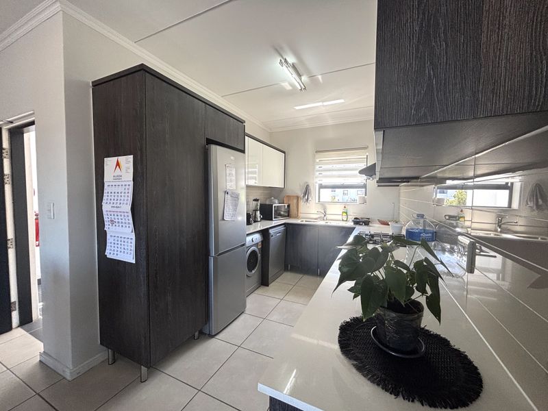 A modern kitchen featuring dark wood cabinetry, stone countertops, tiled flooring, and integrated appliances, offering a functional and well-maintained workspace.