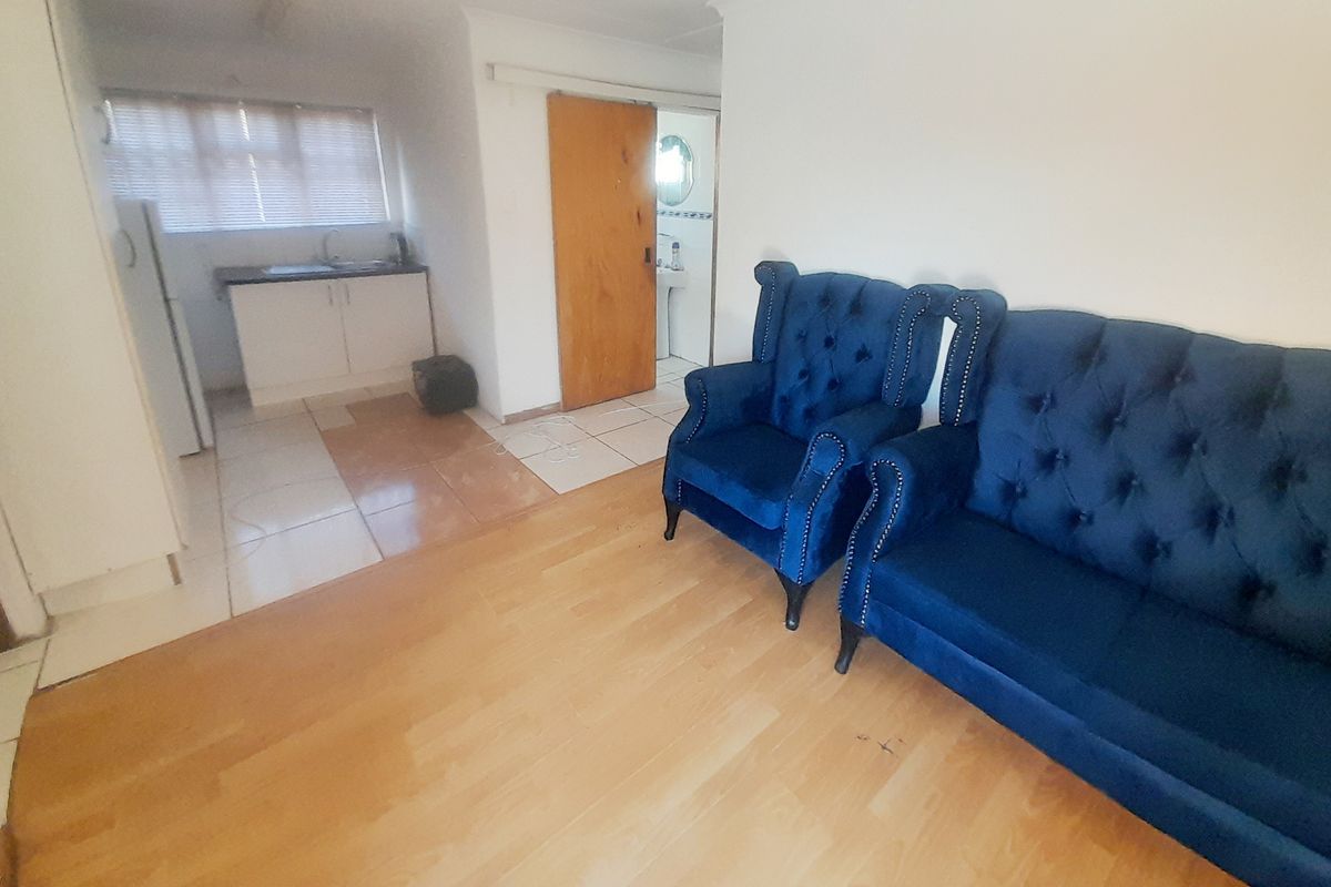 Open plan living area featuring laminate flooring, adjacent kitchen space with cabinetry, and access to a bathroom.