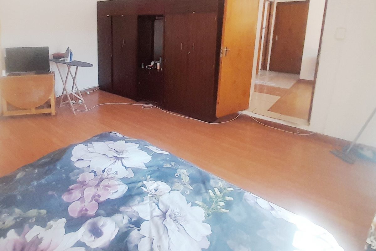 A bedroom featuring laminate flooring and a built-in wooden wardrobe, with an open doorway leading to an adjacent hallway.