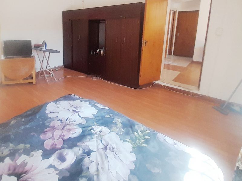 A bedroom featuring laminate flooring and a built-in wooden wardrobe, with an open doorway leading to an adjacent hallway.