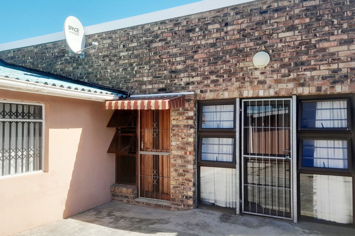 Rear exterior view of the apartment featuring face brick walls, security gates, and a concrete patio area.