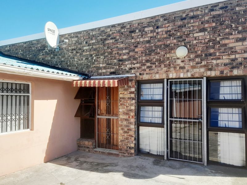 Rear exterior view of the apartment featuring face brick walls, security gates, and a concrete patio area.