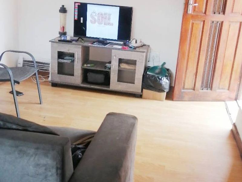 A living room area featuring light-toned laminate flooring and a traditional timber door, providing a functional and neutral base for interior design.