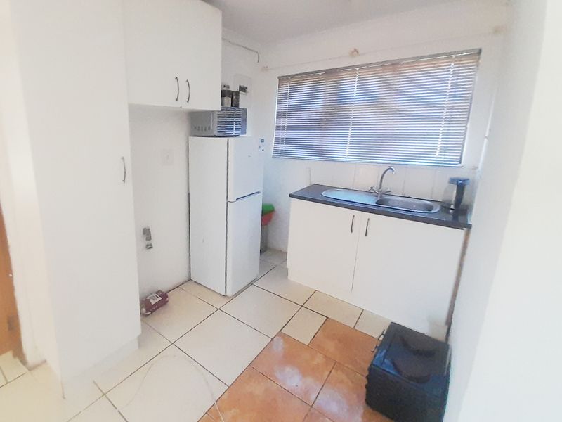 A compact kitchen featuring white cabinetry, a stainless steel sink, and mixed floor tiling, requiring cosmetic updates to improve its overall appeal.