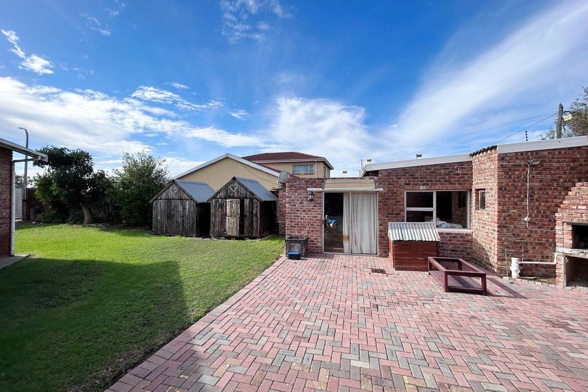 Rear exterior view featuring a brick-paved patio, a grass lawn, and a built-in outdoor braai area, providing a functional space for outdoor living.