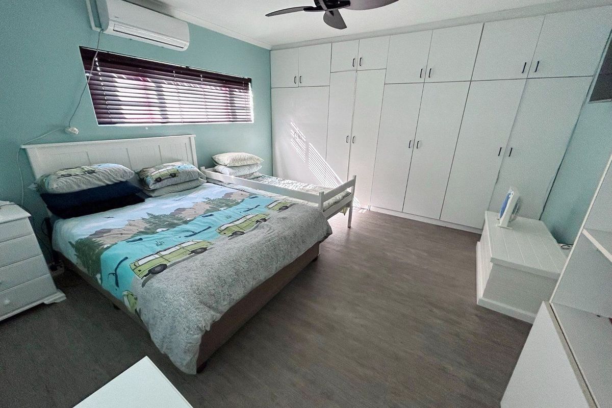 Spacious bedroom featuring extensive built-in cabinetry, a wall-mounted air conditioning unit, and a ceiling fan, finished with modern wood-look flooring.