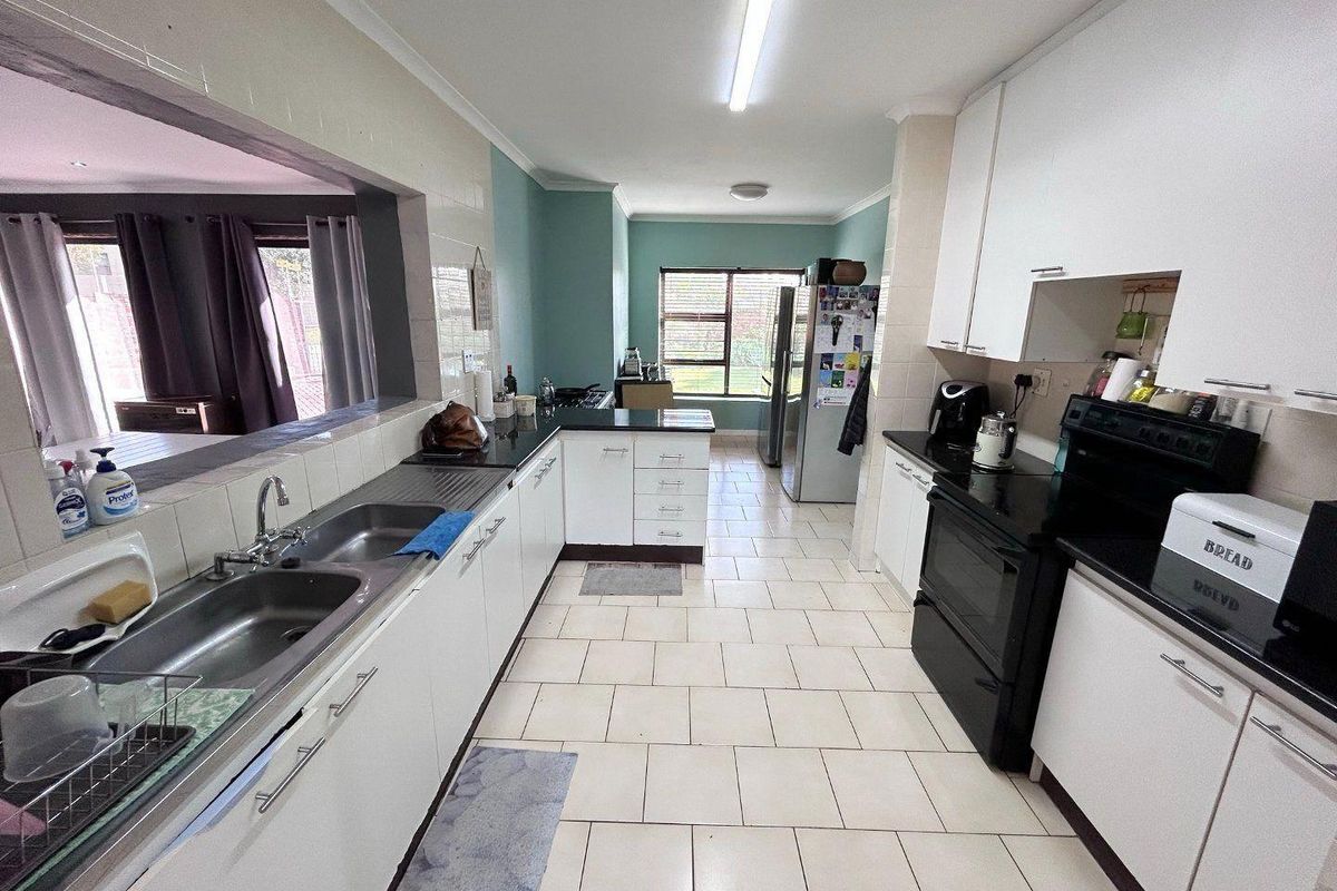 Functional kitchen featuring white cabinetry, dark countertops, double stainless steel sink, and tiled flooring with a convenient serving hatch to the living area.