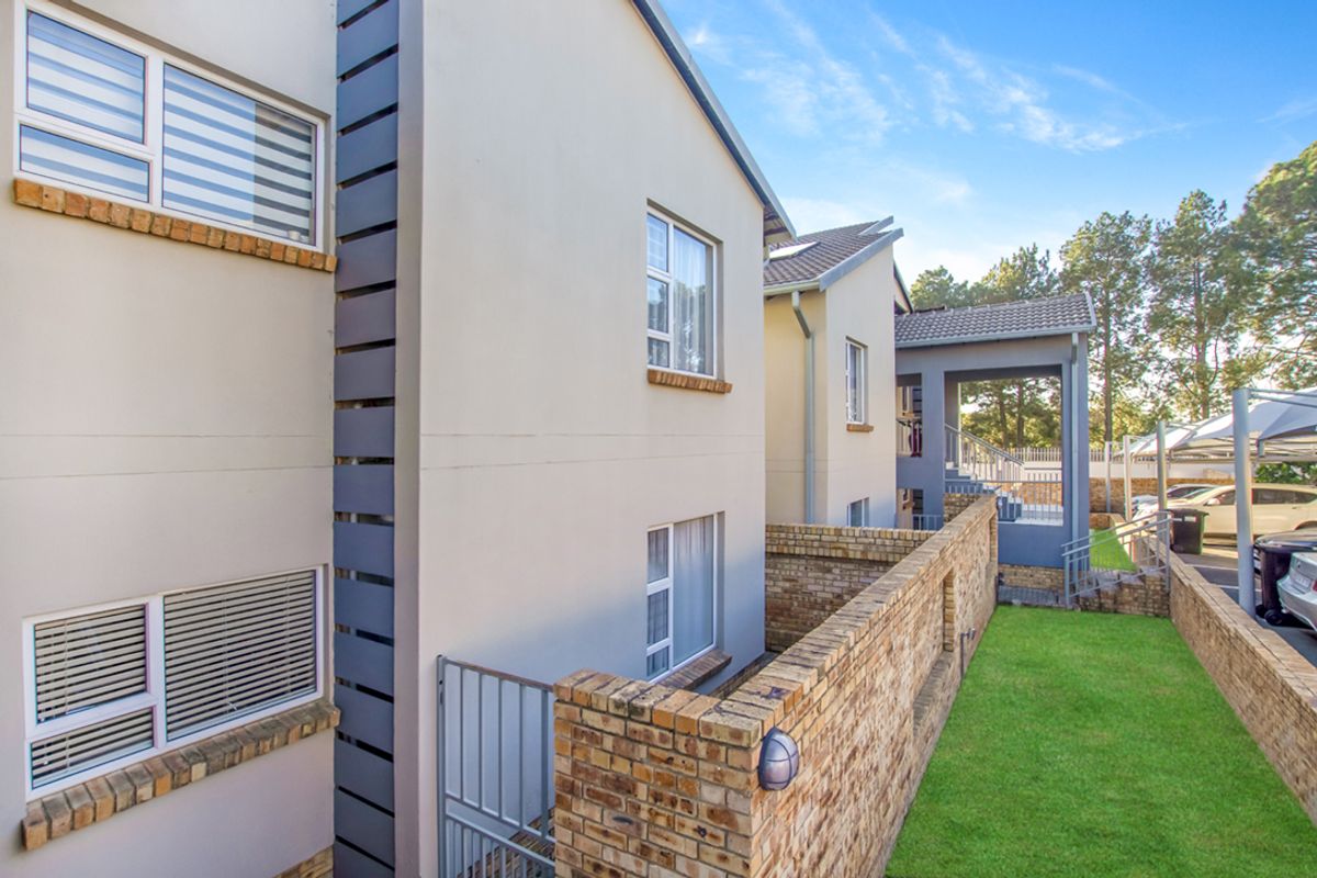 A view of the apartment complex exterior featuring modern facade finishes, brick boundary walls, and a well-maintained lawn area.