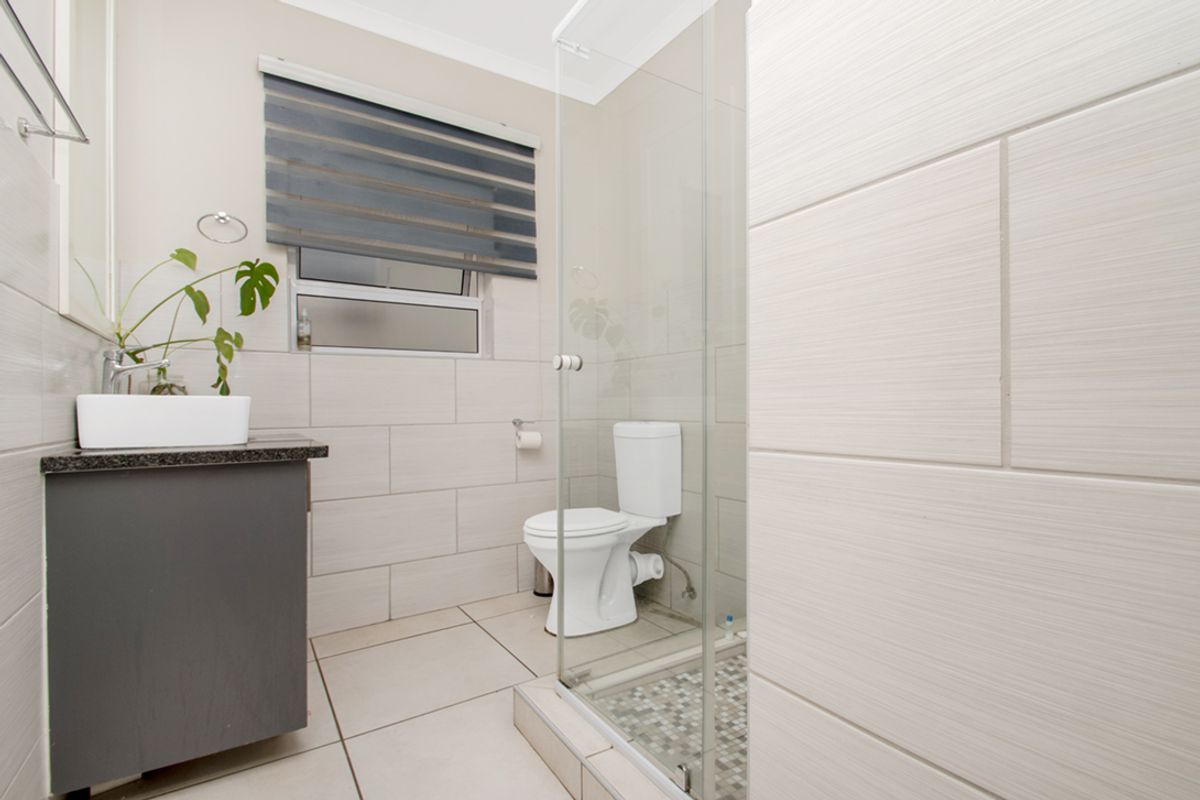 Modern bathroom featuring a glass-enclosed shower, contemporary vanity with vessel sink, and neutral wall tiling.