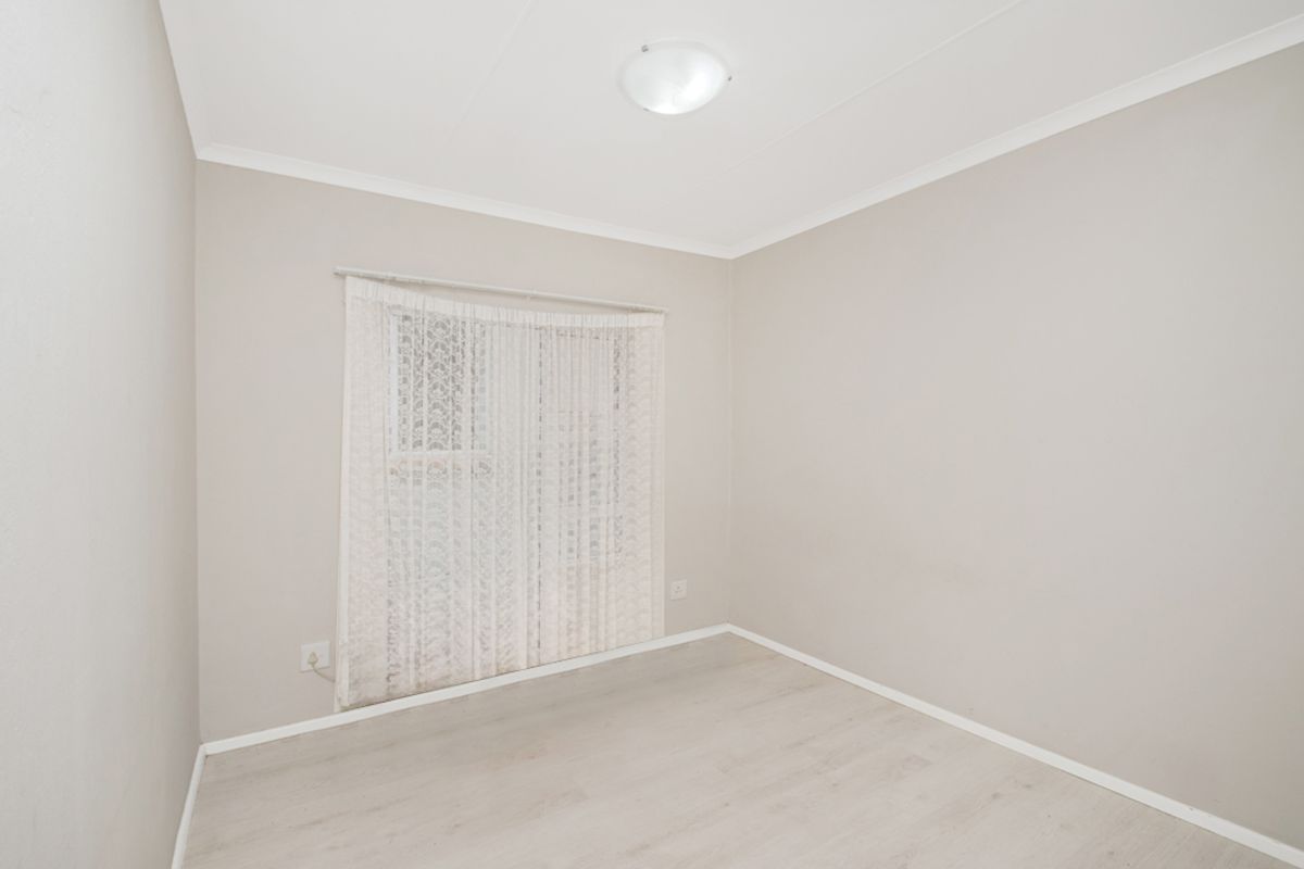 A clean, empty bedroom featuring neutral wall paint, light-toned laminate flooring, and a window with fitted curtain tracks.