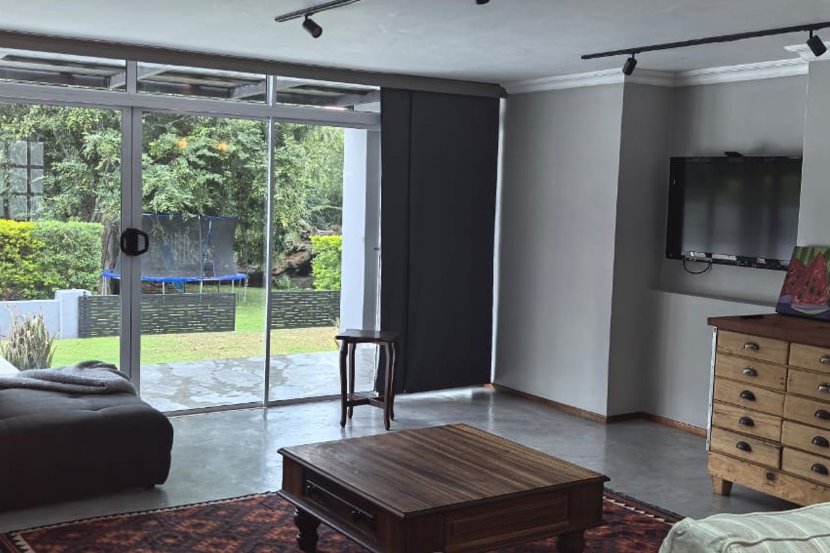 Spacious living room featuring polished concrete floors, track lighting, and large sliding glass doors providing seamless access to the rear garden.
