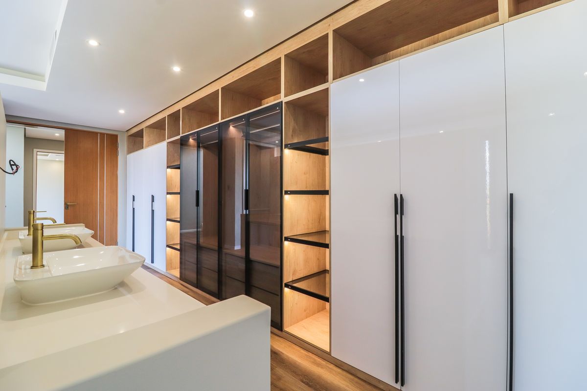 Modern bathroom featuring dual vessel sinks with gold-tone faucets and extensive custom built-in cabinetry with integrated lighting and glass-fronted shelving.