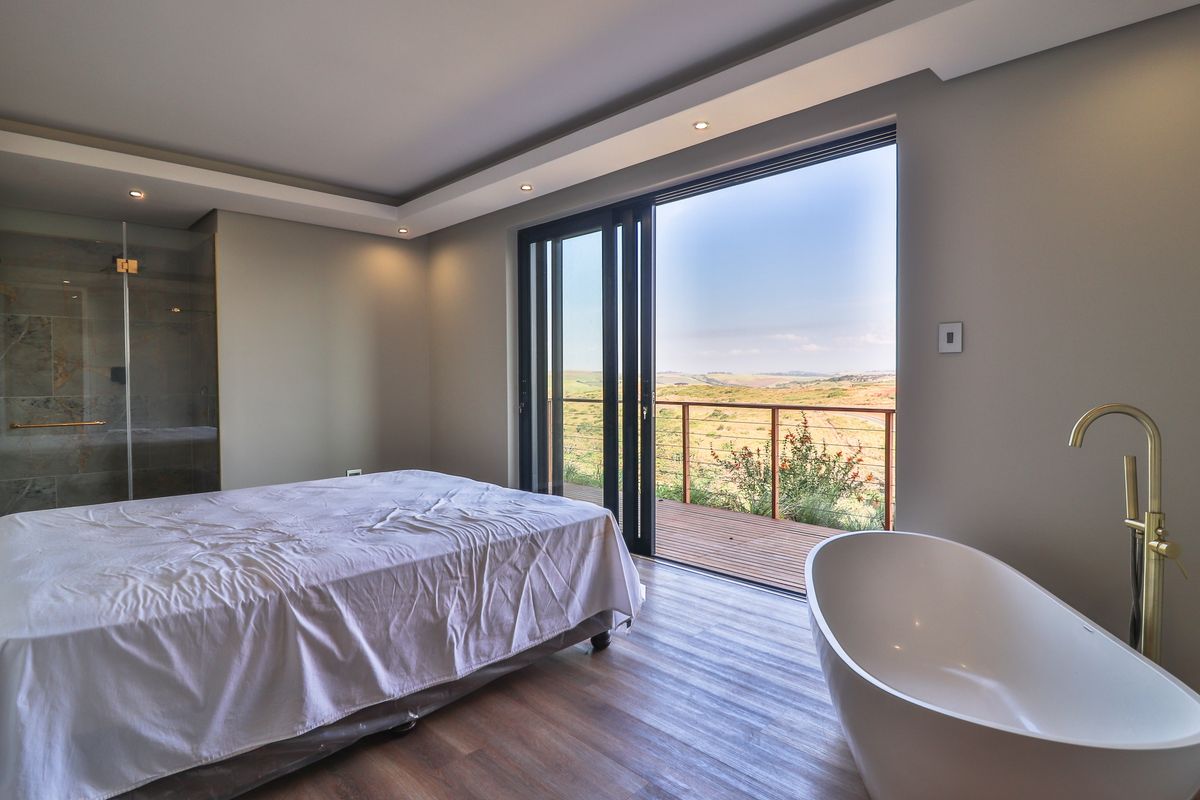 Modern open-plan bedroom featuring a freestanding bathtub, glass-enclosed shower, and large sliding doors opening onto a private balcony with scenic landscape views.