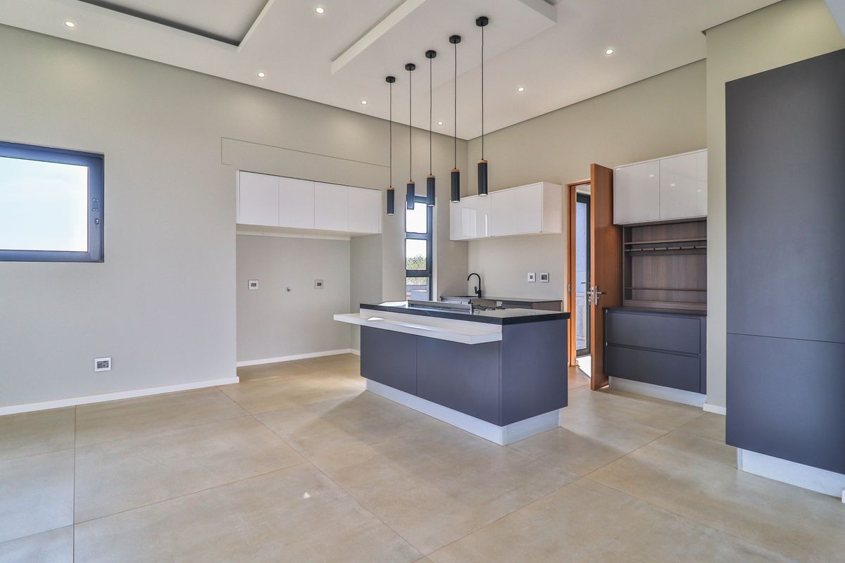 Modern open-plan kitchen featuring a central island with integrated hob, sleek cabinetry, recessed ceiling lighting, and large format floor tiles.