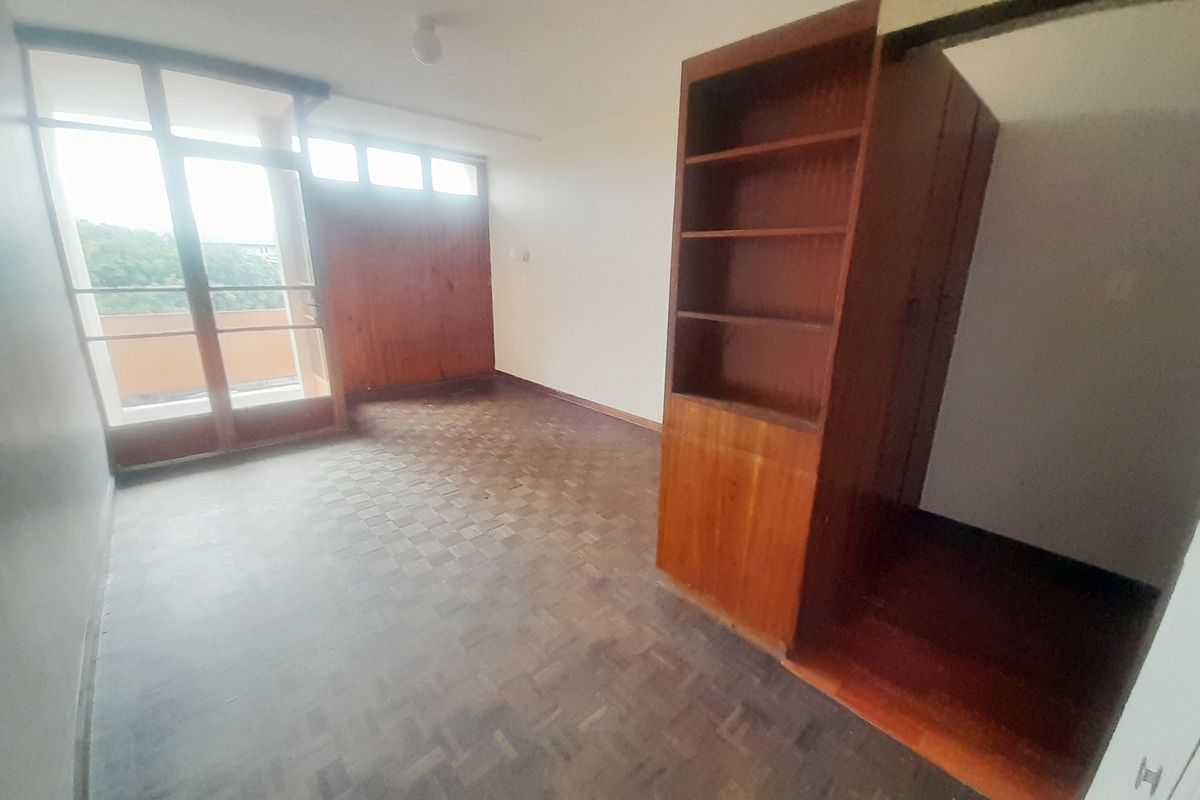 An empty bedroom featuring original parquet flooring, built-in wooden cabinetry, and access to a balcony through a glass-paneled door.