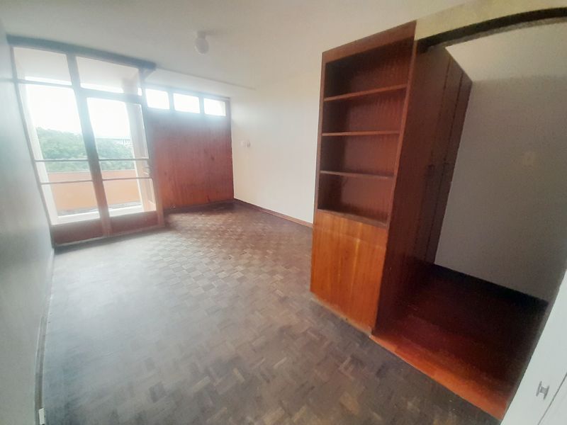 An empty bedroom featuring original parquet flooring, built-in wooden cabinetry, and access to a balcony through a glass-paneled door.