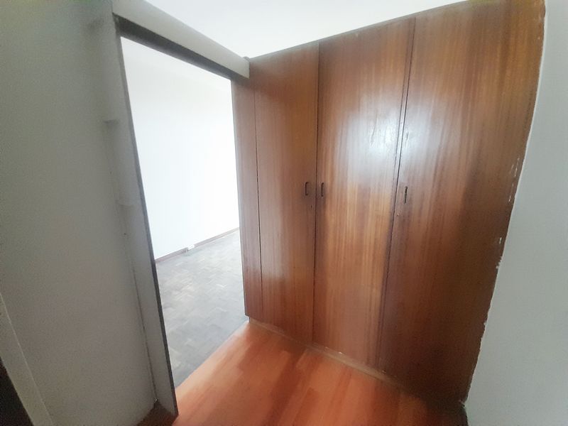 A vacant bedroom featuring built-in wooden cupboards and a combination of parquet and laminate flooring, offering a blank canvas for potential updates.