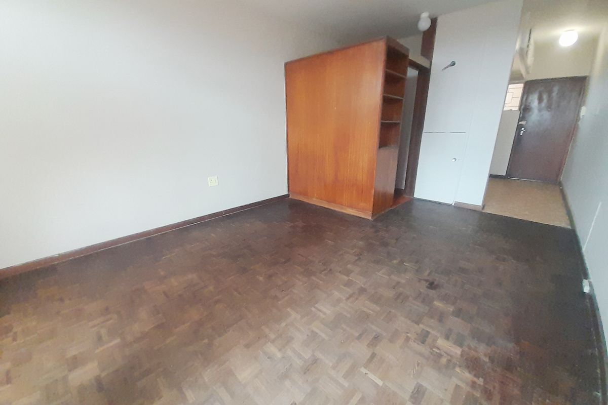 An empty bedroom featuring original parquet flooring and a built-in wooden cupboard, offering a blank canvas for renovation and interior design updates.