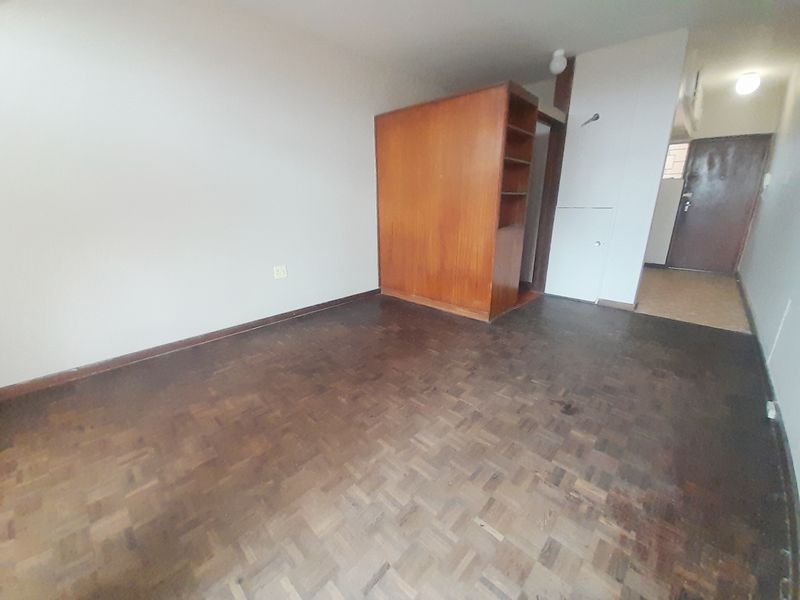 An empty bedroom featuring original parquet flooring and a built-in wooden cupboard, offering a blank canvas for renovation and interior design updates.