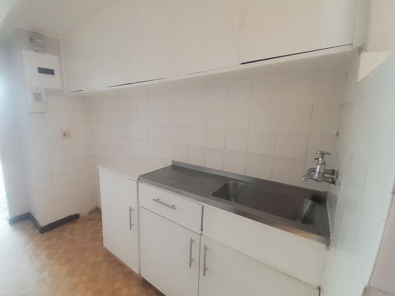 A compact, empty kitchen area featuring basic white cabinetry, a stainless steel sink, and tiled splashbacks, ready for modernization.