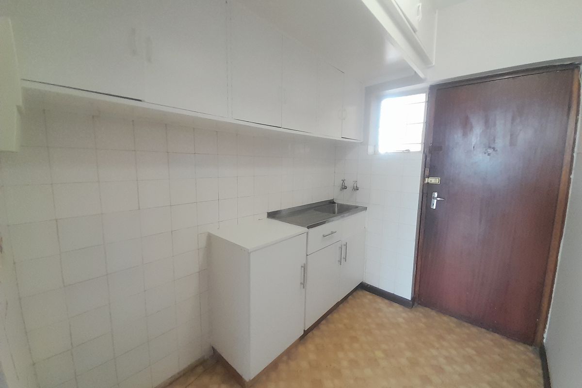 A functional scullery or utility area featuring built-in white cabinetry, a stainless steel sink, and tiled splashbacks, offering potential for modernization.