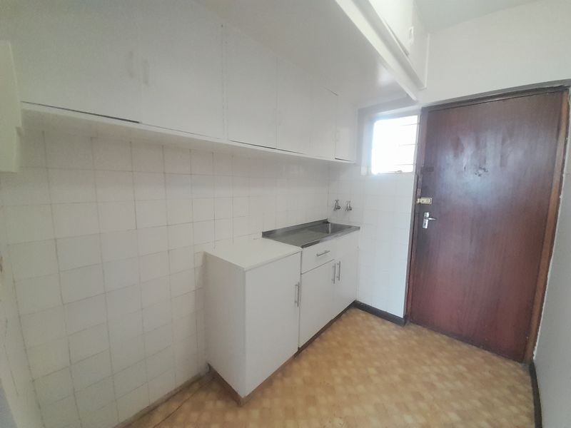 A functional scullery or utility area featuring built-in white cabinetry, a stainless steel sink, and tiled splashbacks, offering potential for modernization.