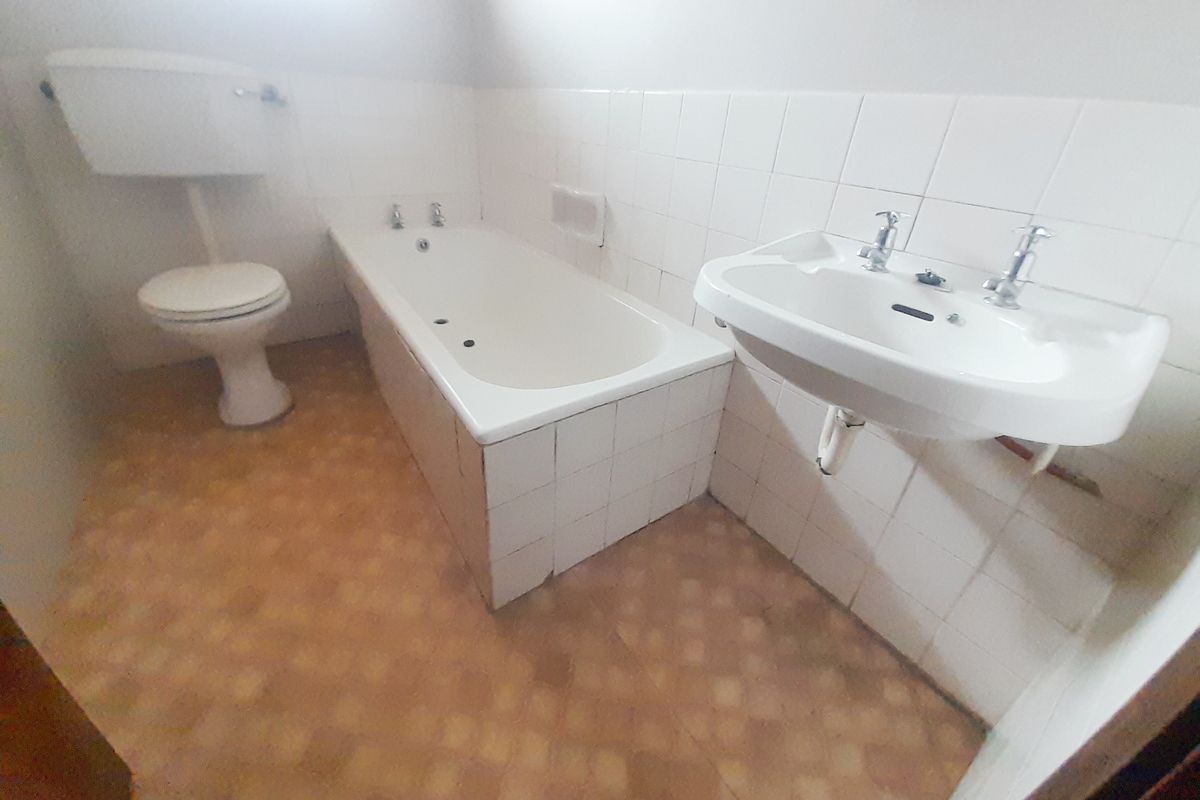 A dated bathroom featuring a standard bathtub, wall-mounted basin, and toilet, requiring modernization of finishes and fixtures.