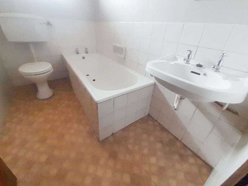 A dated bathroom featuring a standard bathtub, wall-mounted basin, and toilet, requiring modernization of finishes and fixtures.