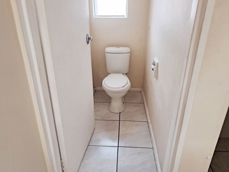 A compact, functional guest toilet featuring tiled flooring and neutral wall finishes, presenting a clean but dated aesthetic.