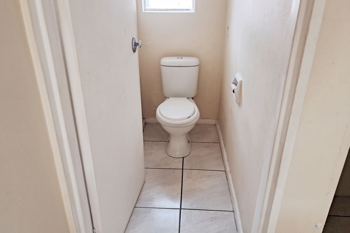A compact, functional guest toilet featuring tiled flooring and neutral wall finishes, presenting a clean but dated aesthetic.