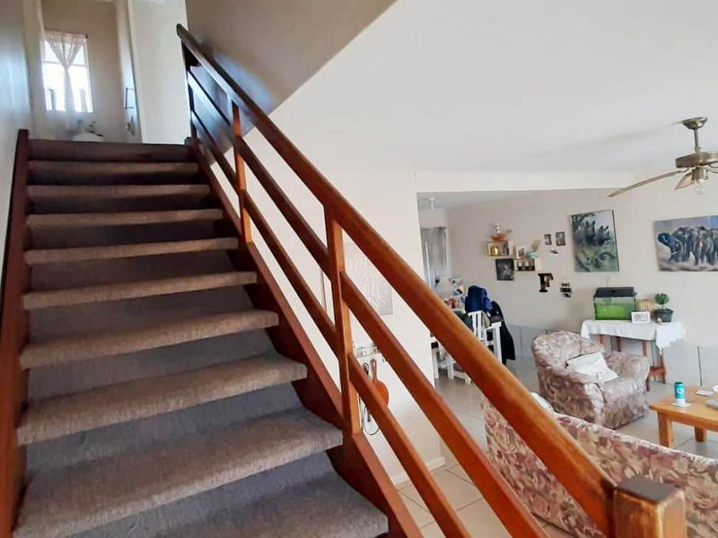 Open plan living area featuring a wooden staircase with a matching handrail and a ceiling fan, connecting the lower level to the upper floor.