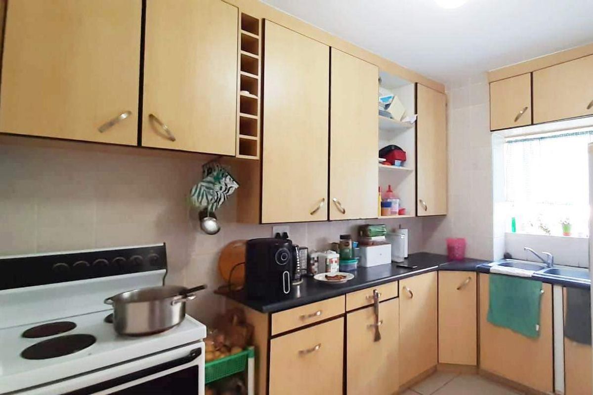 A functional kitchen featuring light wood-tone cabinetry, dark countertops, a double bowl sink, and a freestanding stove with a tiled backsplash.