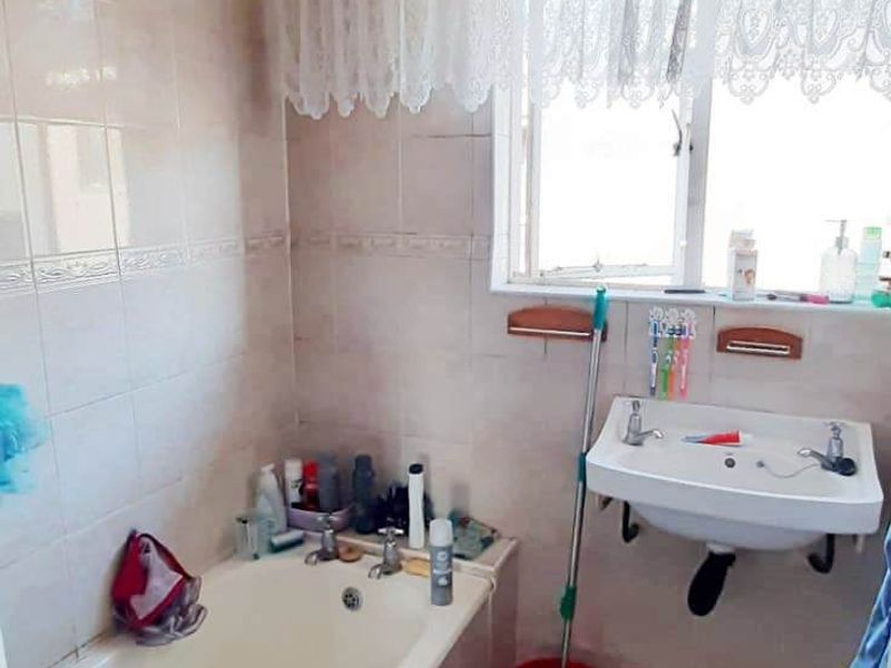 A functional bathroom featuring a bathtub, wall-mounted basin, and neutral wall and floor tiling.